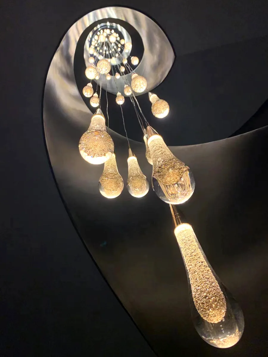 Hand-blown glass teardrop pendants cascading down a black spiral stairwell, photographed looking up